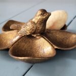 Bronskleurig schaaltje met vogel en wit decoratief element.